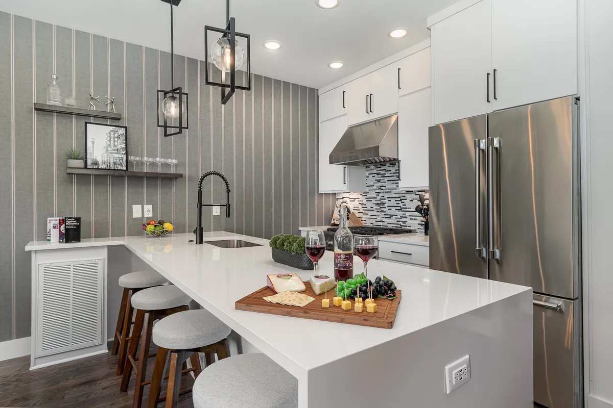 A modern kitchen with an island countertop set for entertaining, complete with wine glasses, a cheese platter, and gleaming stainless steel appliances in the background. The mood is welcoming and sophisticated—perfect for group breakfasts or casual drinks.