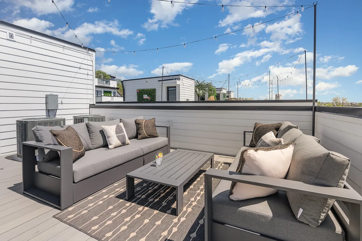 A cozy outdoor seating area adorned with decorative cushions and a central coffee table, all under twinkling string lights. The setting suggests a space perfect for relaxed socializing, morning coffee rituals, or quiet evening reflections—elevated by a strong sense of privacy and comfort.