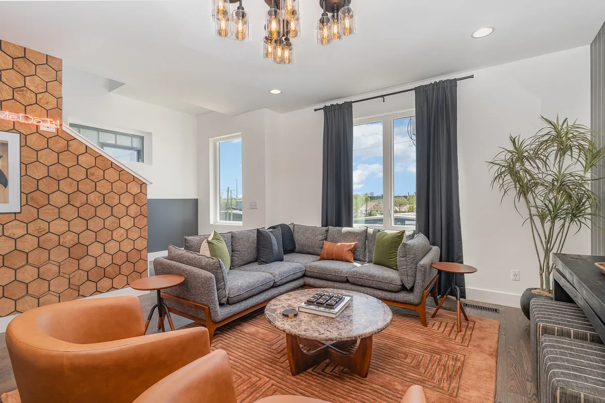 A spacious living room with a large sectional sofa arranged around a chic coffee table, set against a striking hexagonal feature wall. Stylish lighting and modern decor create a welcoming environment ideal for both relaxing and socializing.