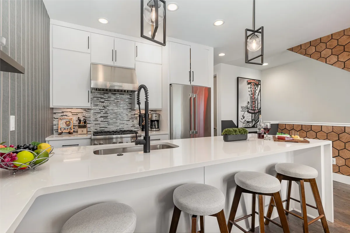 A bright, welcoming kitchen centered around a spacious island adorned with a colorful fruit bowl. Pendant lights create a warm atmosphere, while modern appliances and ample counter space invite guests to cook or gather as a family.
