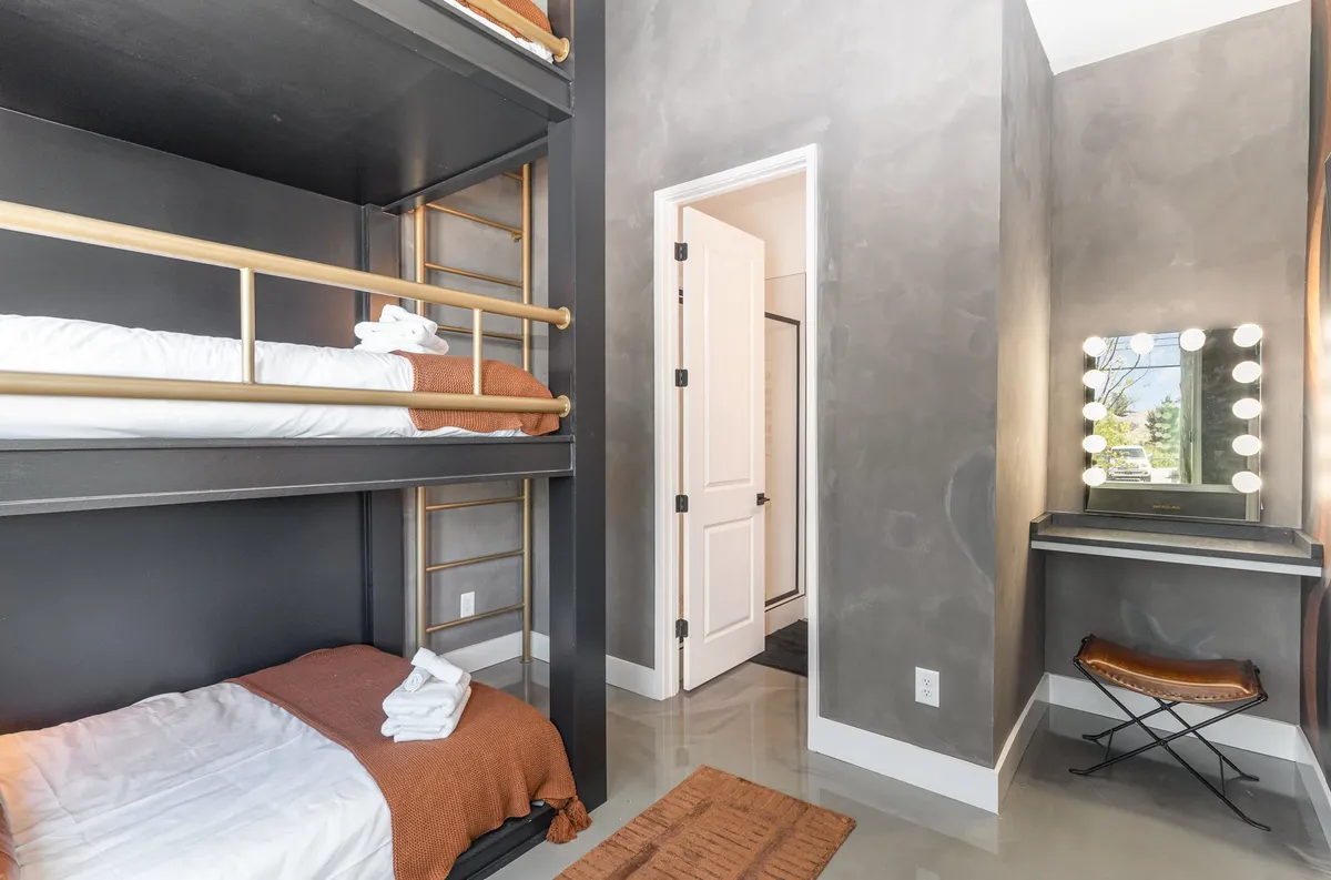 Bunk beds with a vanity mirror and an entryway door visible. The room is functional, inviting, and designed for both restful sleep and getting ready, supporting group dynamics and morning routines.