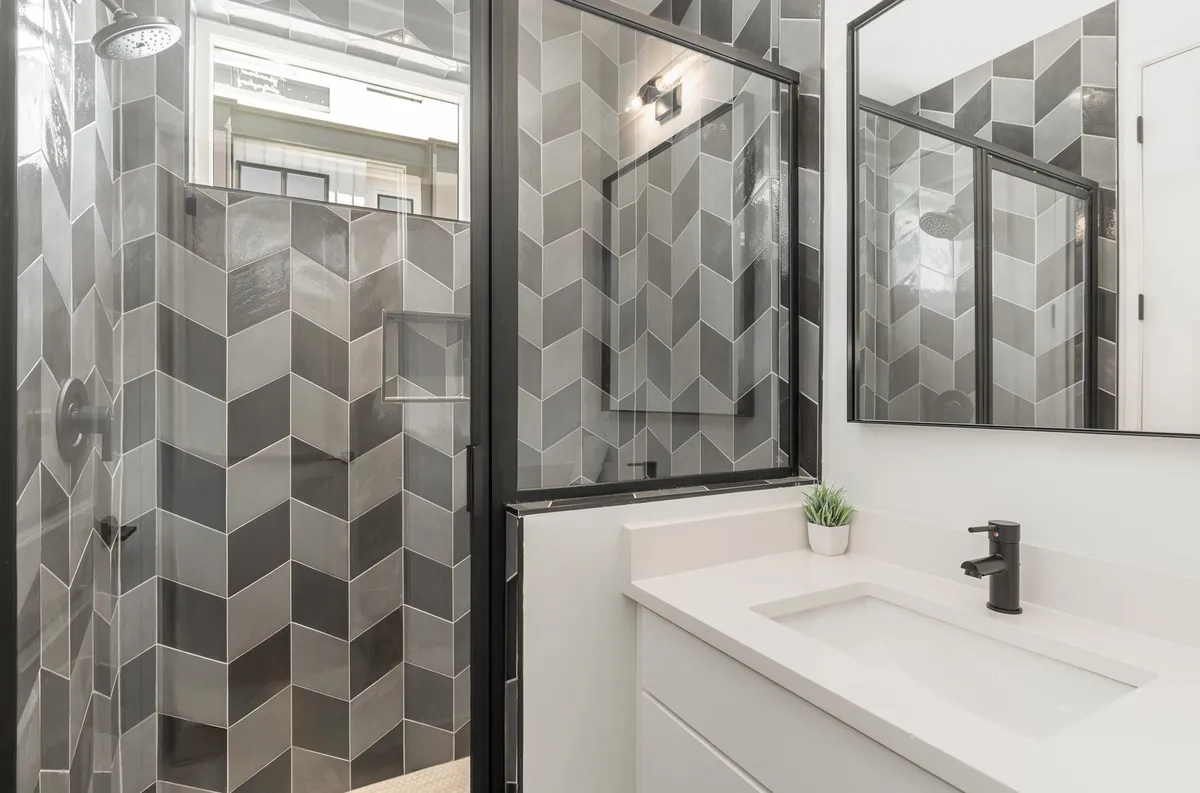 A stylish bathroom with hexagon-patterned shower walls, a sleek vanity with a modern faucet, and a mirror that reflects natural light. The setting feels fresh and rejuvenating.
